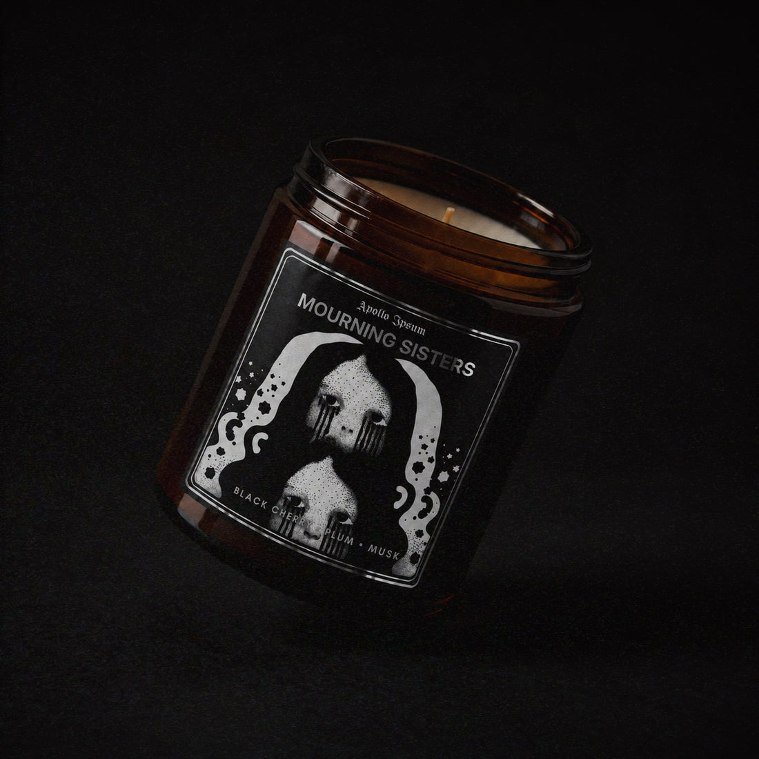 Mourning Sisters soy wax candle in an amber jar with illustrated label, Apollo Ipsum Things That Shouldn&