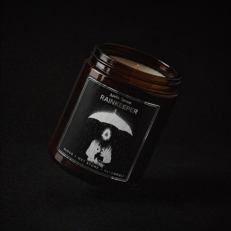 Rainkeeper soy wax candle in an amber jar with illustrated label, Apollo Ipsum Things That Shouldn't Exist collection